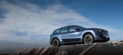 BMW iX3 in Blau, schräg von vorne aufgenommen, steht auf einem Felsen vor blauem Himmel und vermittelt moderne elektrische Mobilität und sportliches Design.