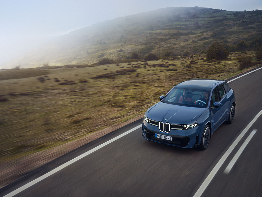 Neuer BMW iX3 der Neuen Klasse, vollelektrisches SUV fährt auf Landstraße durch hügelige Landschaft