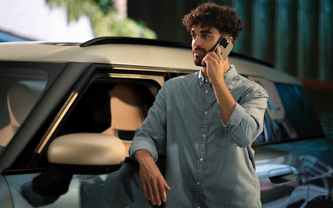 Mann lehnt an einem MINI und telefoniert mit dem Smartphone, im Hintergrund urbane Umgebung bei Tageslicht.